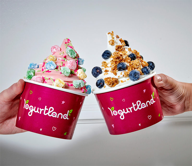 Hands holding two cups of Yogurtland frozen yogurt.