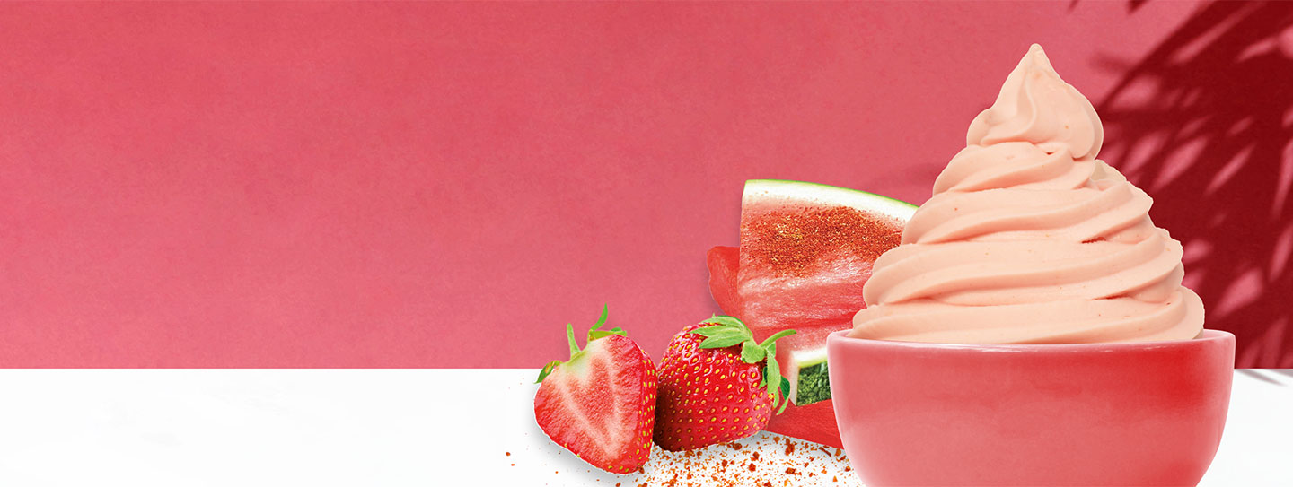 A cup of frozen yogurt alongside strawberries and watermelon slices.