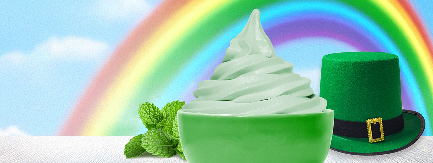 A cup of frozen yogurt alongside a sprig of mint and green top hat.