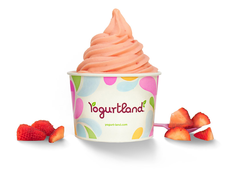A cup of Yogurtland frozen yogurt alongside cut strawberries